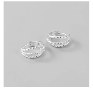 Macro detail of S925 sterling silver triple-layer twisted hoop earrings on grey base