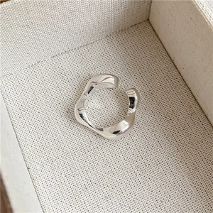 Close-up of a minimalist silver irregular wavy open ring on a textured jewelry cushion