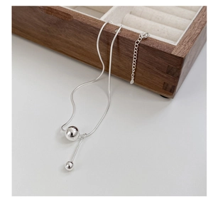 Close-up of a 925 silver snake chain necklace with polished beads on a wooden box
