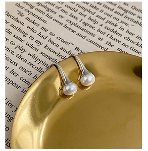 Détail de boucles d'oreilles bicolores avec perle blanche sur fond de livre vintage