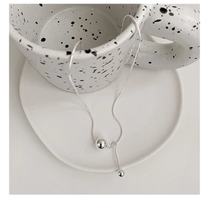 Detail shot of s925 silver snake chain with dual spherical pendants on ceramic plate