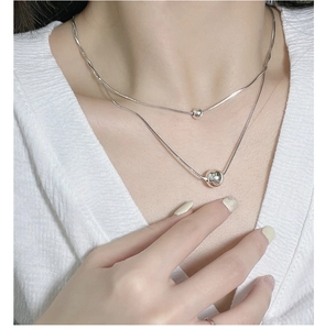 Detail of double-layered silver snake chain necklace featuring polished spherical pendants