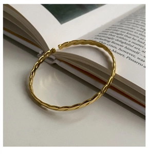 Macro shot of minimalist gold twisted open cuff bracelet on a white minimalist background