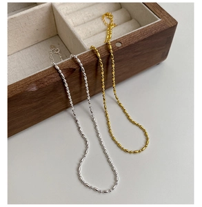 Détail de colliers à perles olive argentés et dorés sur un coffret en noyer