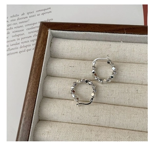Macro detail of silver geometric stud hoop earrings on a linen jewelry display box