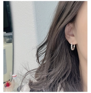 Macro view of sterling silver huggie earrings with textured faceted design on ear
