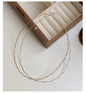 Detailed close-up of gold and silver S925 sterling silver wave necklaces on white surface