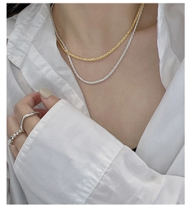 Detail of layered gold and silver twisted rope chains and textured rings on a model