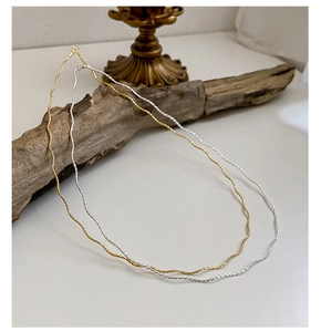 Detail of wavy textured gold and silver chains draped over natural wood for a minimalist look