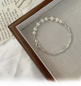Detail of silver wavy bangle with baroque pearl clasp on minimalist linen display
