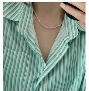 Détail d'un collier de perles colorées avec touches dorées sur une chemise