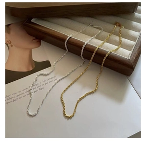 Close-up of gold and silver twisted rope chains on a wooden jewelry tray with lobster clasp