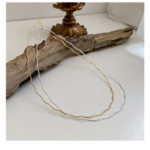Detailed view of silver and gold wavy necklaces showing textured metallic surface on wood