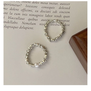 Dettaglio di anelli d'argento con trama irregolare, perla bianca e design a lava