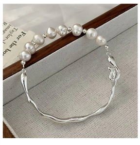 Macro detail of irregular silver stream-line bangle with elegant baroque pearls
