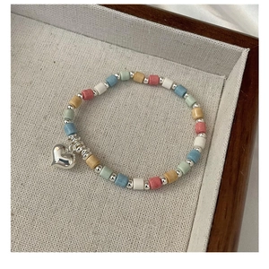 Macro view of rainbow beaded necklace with a polished silver heart pendant on a linen tray