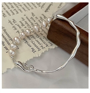 Macro detail of irregular silver bracelet featuring polished freshwater pearls and metal wave
