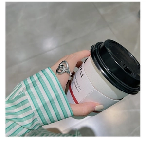Close-up of S925 sterling silver interlocking twist ring on finger with coffee cup