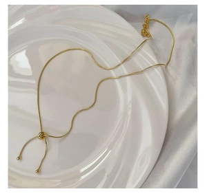 Detail of gold snake chain necklace with adjustable slider bead on ceramic tray