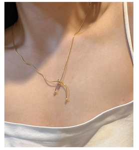 Detail of a golden snake chain necklace featuring a minimalist U-shaped knot pendant