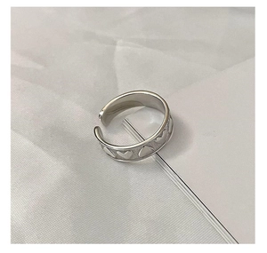 Detailed close-up of adjustable silver heart ring with embossed pattern on matte texture