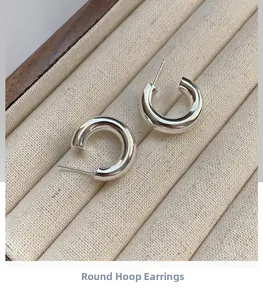 Macro view of chunky silver C-shape hoop earrings on a textured linen jewelry display