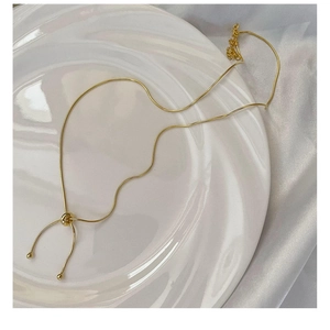 Detail of adjustable golden snake chain necklace with sliding bead on white ceramic tray