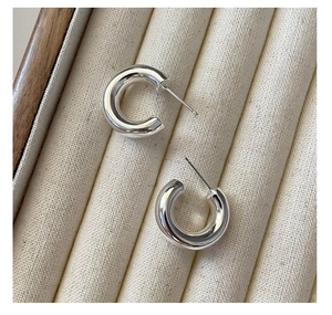 Close-up of polished S925 sterling silver C-shaped hoop earrings on beige velvet tray