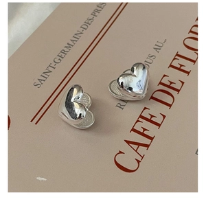 Close-up of S925 sterling silver heart studs with a polished mirror finish on beige card
