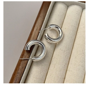 Close-up of chunky silver C-shape hoop earrings with high-polish finish on velvet tray
