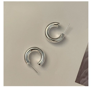 Macro detail of glossy S925 sterling silver C-shaped hoop earrings on a beige background
