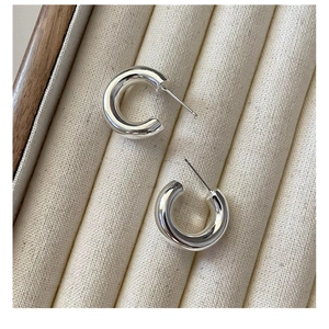 Detailed macro view of polished S925 sterling silver C-shaped hoop earrings on fabric