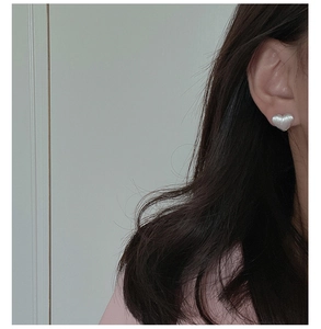 Detail of a white heart-shaped pearl stud earring worn on the earlobe with soft lighting