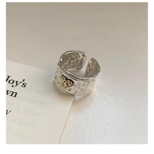Macro shot of silver hammer-textured wide ring with small gold heart detail