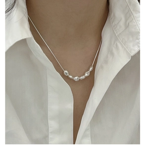 Detailaufnahme von unregelmäßigen Silberperlen an einer feinen Kette auf weißem Hemd