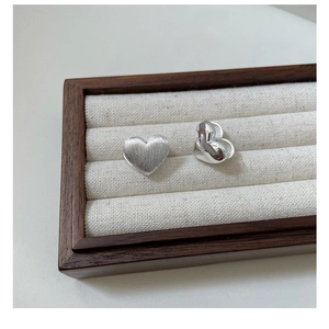 Detail of heart silver earrings showing brushed matte and polished dual textures on a tray