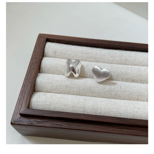 Macro detail of S925 sterling silver heart and H-shaped studs with brushed matte finish