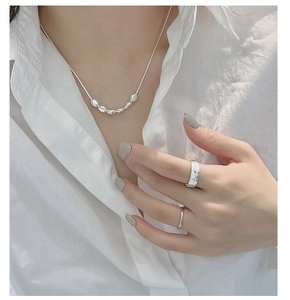 Makroaufnahme von Silberperlenkette und minimalistischen Ringen auf weißem Hemd