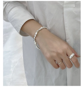 Nahaufnahme von silbernem Perlenarmband und Ringen an Model in weißem Hemd