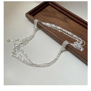 Detailed view of layered S925 sterling silver chain necklace with polished sequins on wood