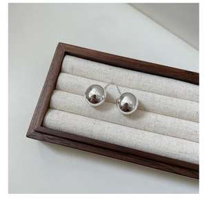Macro view of polished S925 sterling silver ball stud earrings on a wooden tray