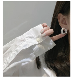 Macro side view of a minimalist brushed silver C-shaped earring on a female model
