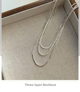 Close-up of triple-layered S925 silver necklace with textured snake chain on beige linen