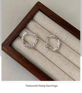 Macro shot of S925 silver hoop earrings with irregular hammered texture on wood background