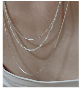 Close-up of layered silver snake chains and textured necklace on woman neck