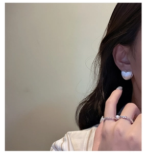 Detailed close-up of a white heart-shaped earring and a minimalist pearl bead ring