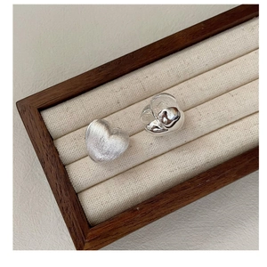 Detail of heart-shaped S925 silver earrings with brushed and polished metal textures