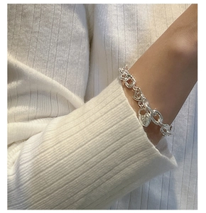 Dettaglio del bracciale a catena con ciondoli a cuore e lucchetto indossato su maglione