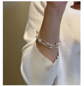 Close-up of a layered S925 sterling silver beaded bracelet on a white knit sleeve