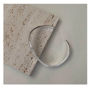 Polished S925 sterling silver minimalist curved bangle on a natural stone background